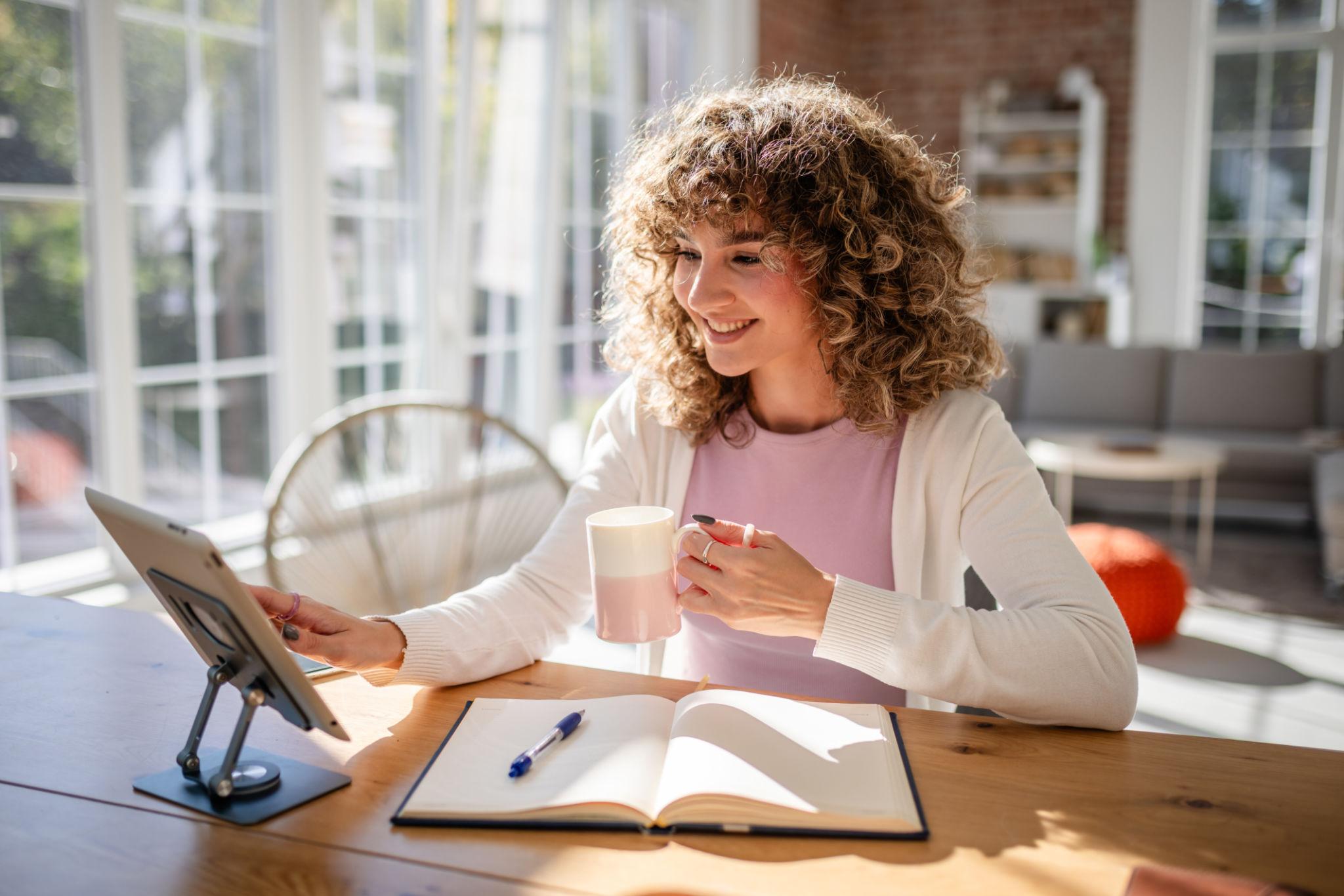 Young Lady Working From Homw Tablet, notebook, and coffee on a wooden table in a warm, inviting home setting