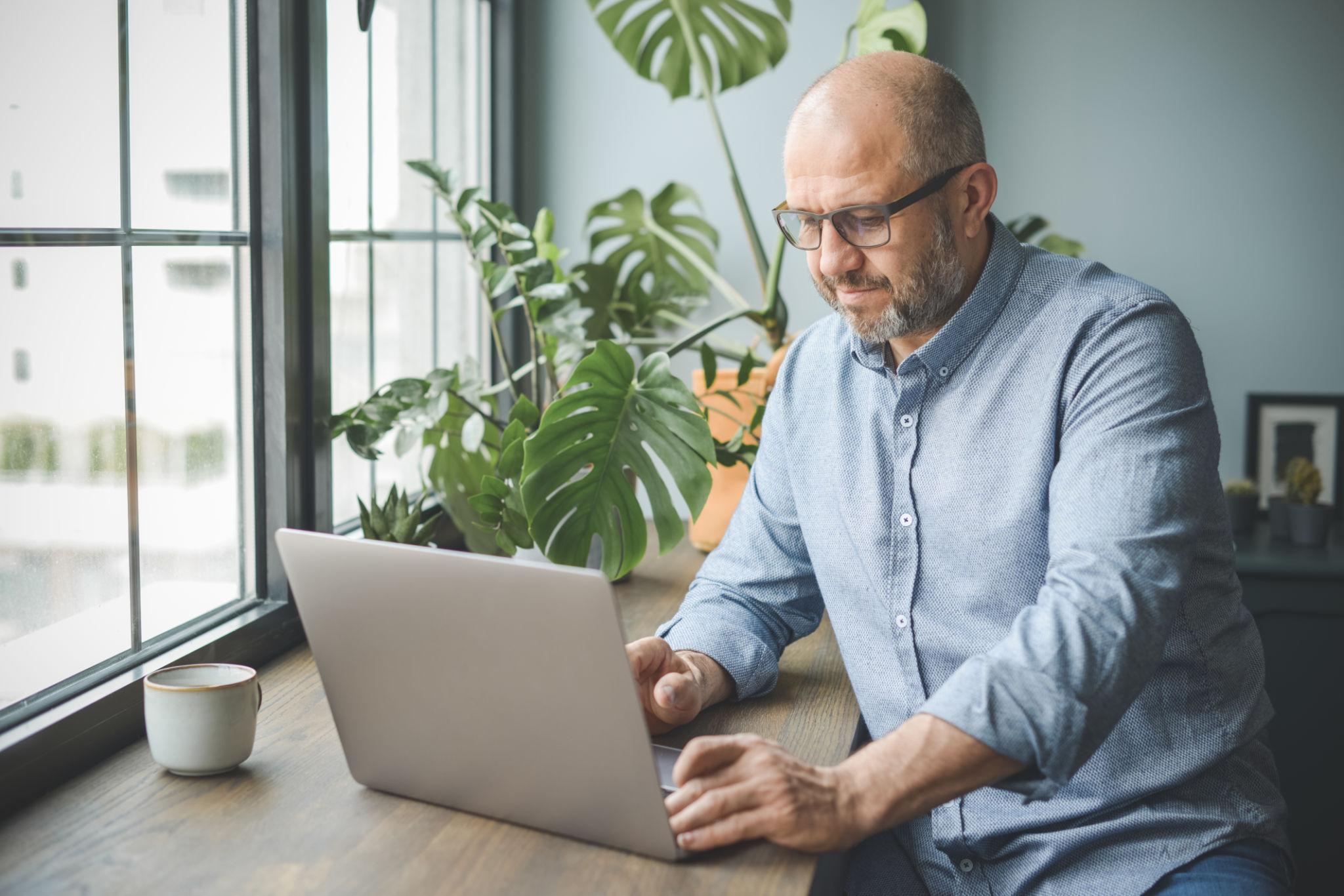 Man on Laptop Adult entrepreneur working on a laptop in a bright home office with plants